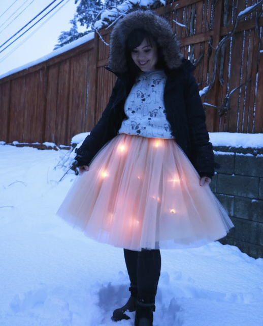 Sophy Wong stoof outside in the snow wearing a black coat with a furry hood and a light pink skirt lit from the inside with L E D lights