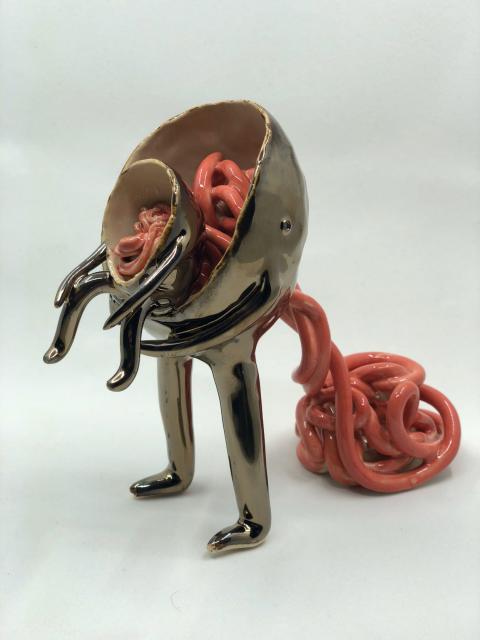 A ceramic sculpture of a gold creature filled with pink noodles, holding a smaller creature 