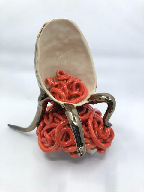 A ceramic sculpture of a creature sitting on a pile of pink noodles