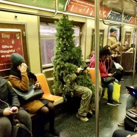 Person dressed as a Christmas tree sitting in a subway car. 