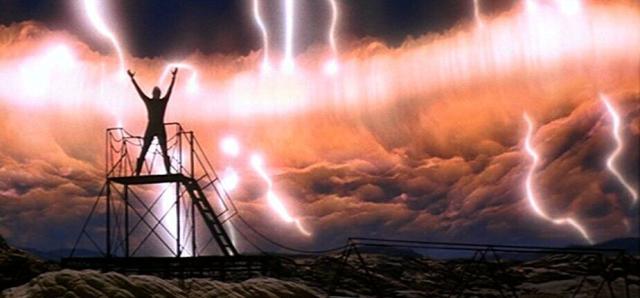 A person stands on a scaffold, arms raised toward an approaching storm