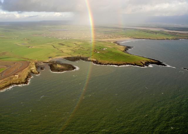 Partial full-circle rainbow in a showery sky over a coastal scene, brightly lit by low midwinter sun.