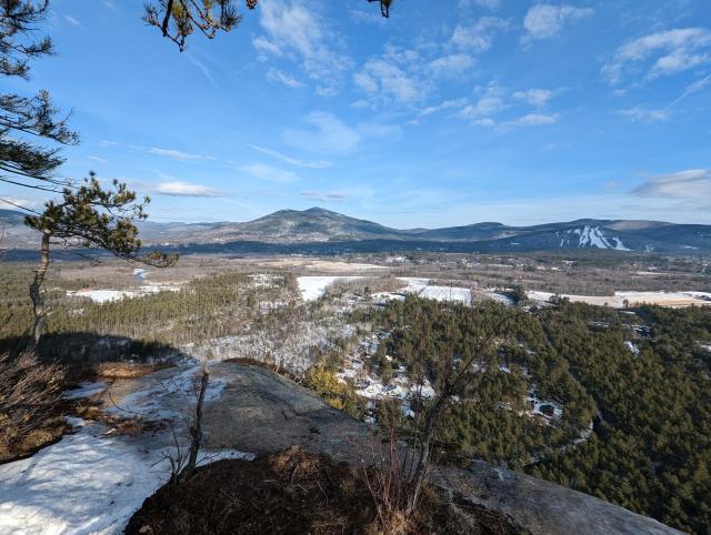 A view from Cathedral Ledge in New Hampshire's White Mountains. Mountains rise up in the distance, while the foreground is miles of forest dotted with towns and winding roads. You can see into tomorrow 