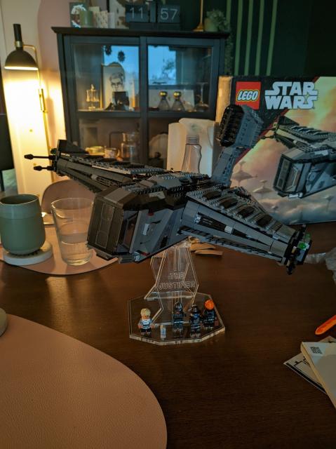 The Lego Star wars ship "the justifier" on a see through pedestal. The justifier is a somber colored, bulky, square adjacent (as much as squares can fly) bounty hunter ship