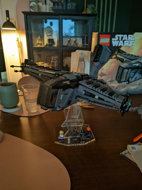 The Lego Star wars ship "the justifier" on a see through pedestal. The justifier is a somber colored, bulky, square adjacent (as much as squares can fly) bounty hunter ship