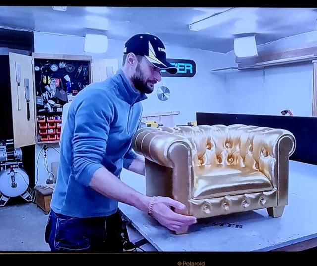 Guy from a YouTube channel called Chester standing next to a small gold upholstered Chesterfield seat he has just made