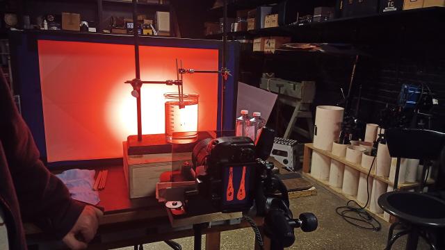 A red screen with a polarizer and quarter wave plate, a receiver with similar, and a breaker with mineral oil and two Prince Rupert's Drops, the left one with the sides ground down. A much nicer camera is seen in the foreground that is nicely focused on the received image with stress bands.