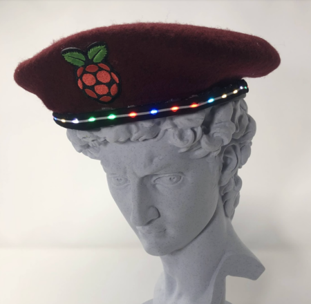 Grey 3D printed classical bust wearing a burgundy beret with an embroidered Raspberry Pi logo and L E D trim