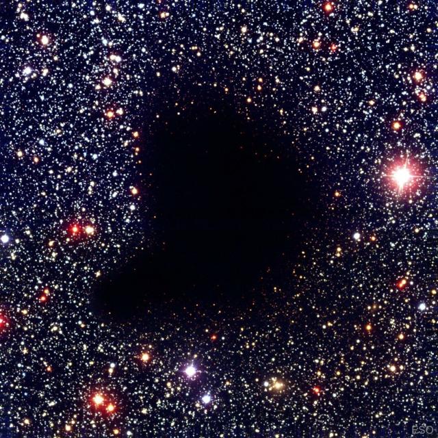A dark comma-shaped cloud appears in the middle of a dense field of stars. No stars are visible through the center of the cloud.