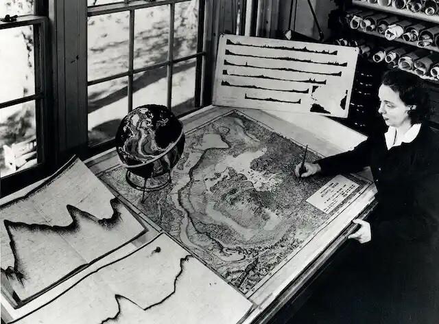 Marie Tharp with an undersea map at her desk. Rolled sonar profiles of the ocean floor are on the shelf behind her. Credit: Lamont-Doherty Earth Observatory and the estate of Marie Tharp