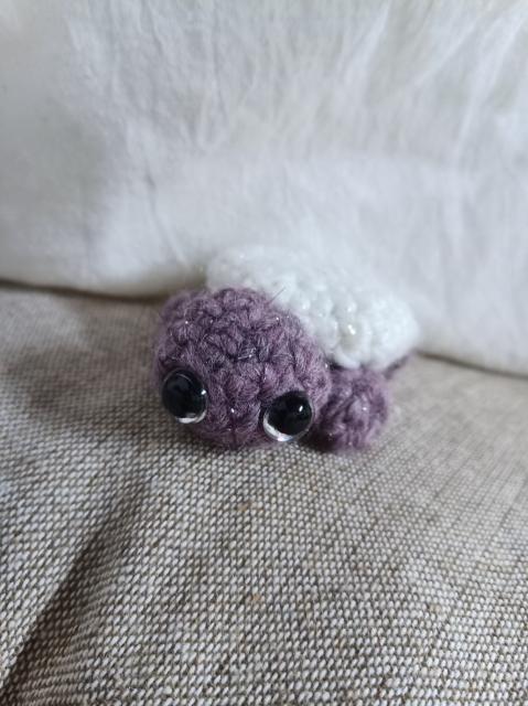 A crochet small (kid hand size) turtle. Its body is purple and the shelf is white.