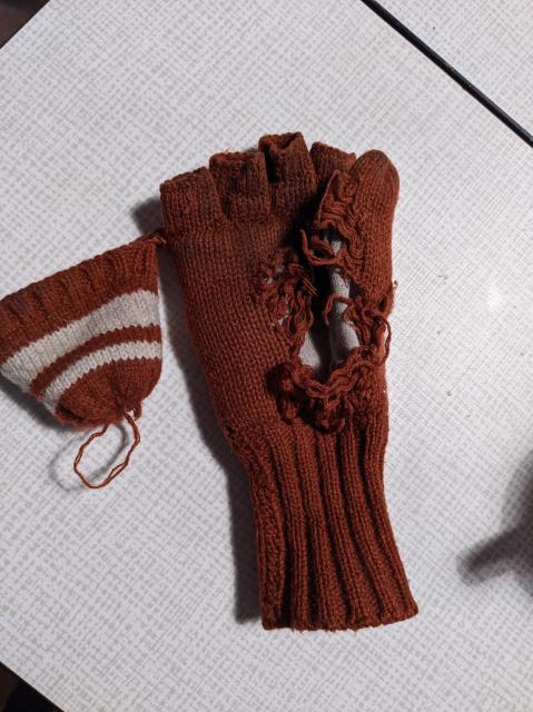 Red brown glove in tatters, the knitted part of the inner hand is almost gone. Only loose threads a and running stitches remain. The glove has an inner fleece part which is intact.