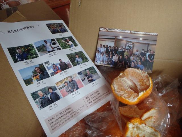 A digital camera photo of a corner of an open box of citrus fruit.  Along with an open  Shirnaui (citrus fruit) half is a a print-out and a photo of the farmers (producers) that make up the group in Minamata responsible for growing the fruits and then finding buyers/eaters for all the great citrus.  