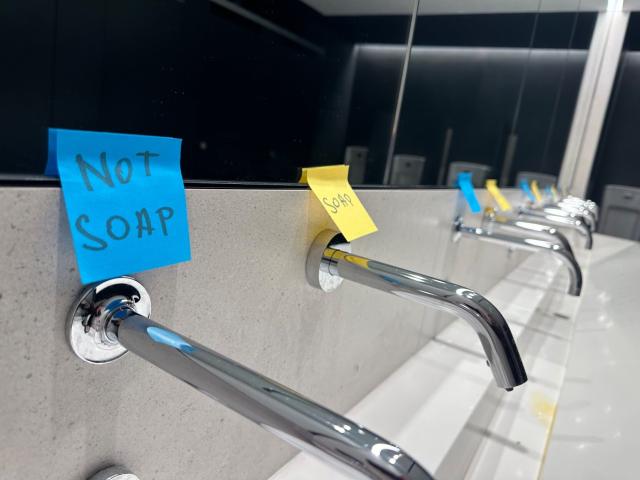 The same backsplash as the other image from an angle that reveals 4 more pairs of spigots receding into the background, all bearing the same pair of color-coded post-its.
