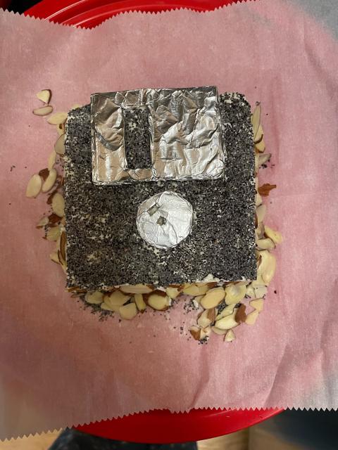 A cheese ball made to look like a 3.5” floppy disk, decorated with foil, poppyseeds, and slivered almonds.
